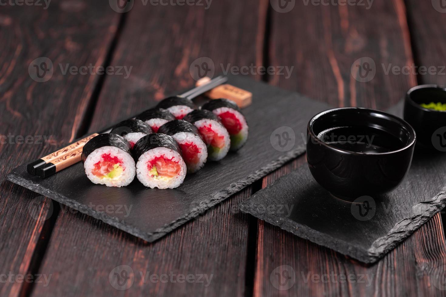 Maki-Sushi-Rolle mit Lachs-Avocado und Tobiko-Kaviar, serviert auf schwarzem Brett, Nahaufnahme - japanisches Essen foto