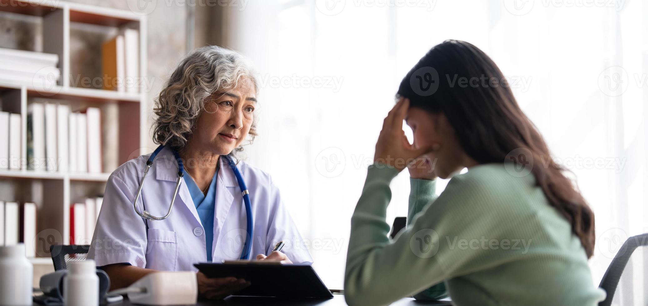Die leitende Ärztin liest die Krankengeschichte der Patientin und spricht mit ihr während der Konsultation in einer Gesundheitsklinik. Arzt im Laborkittel sitzt hinter einem Laptop im Krankenhausbüro. foto