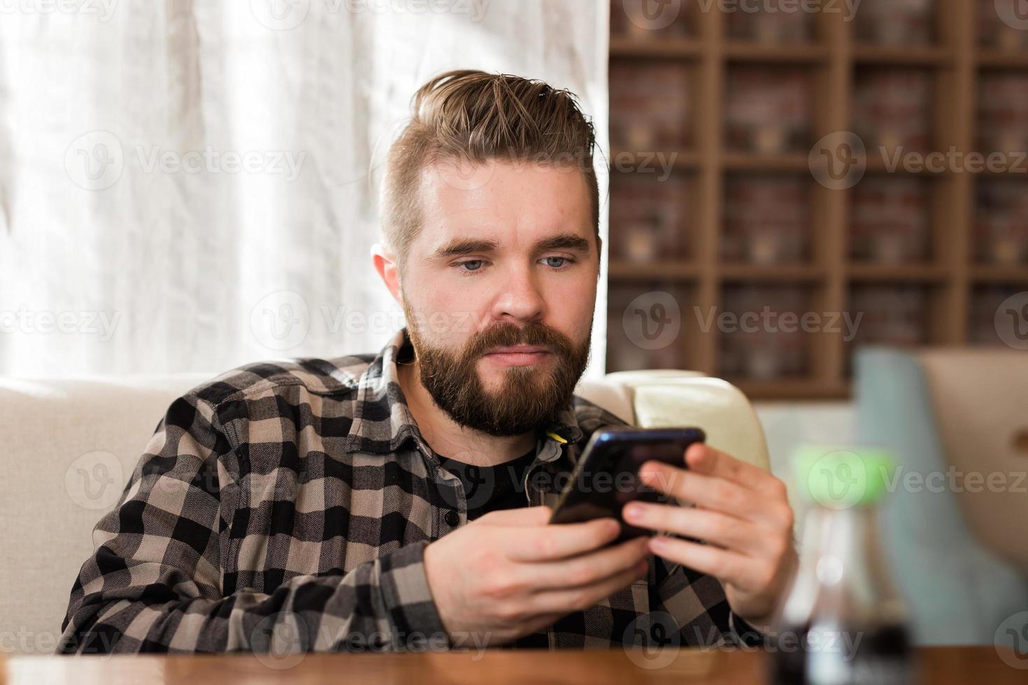 Lächelnder Mann mit Smartphone im modernen Café, er chattet Online-Messaging auf dem Handy. Konzept für soziale Netzwerke und Millennials foto