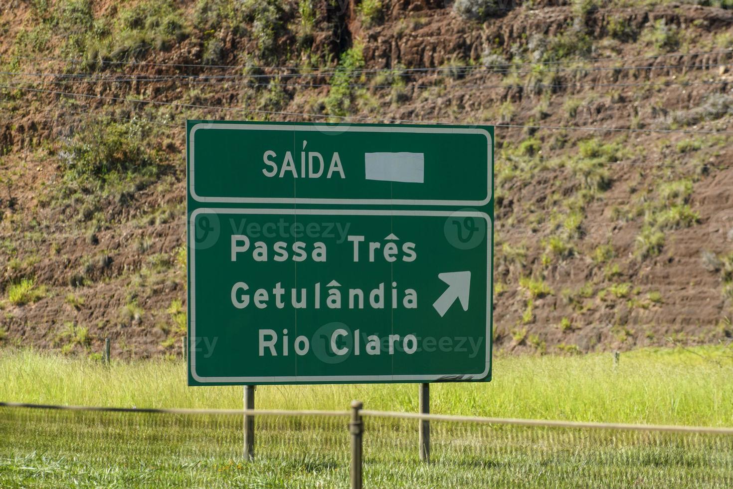 gelbes straßenschild, das die richtung der stadt auf einer straße in brasilien angibt, die eine vorwärtskurve auf einer straße signalisiert foto