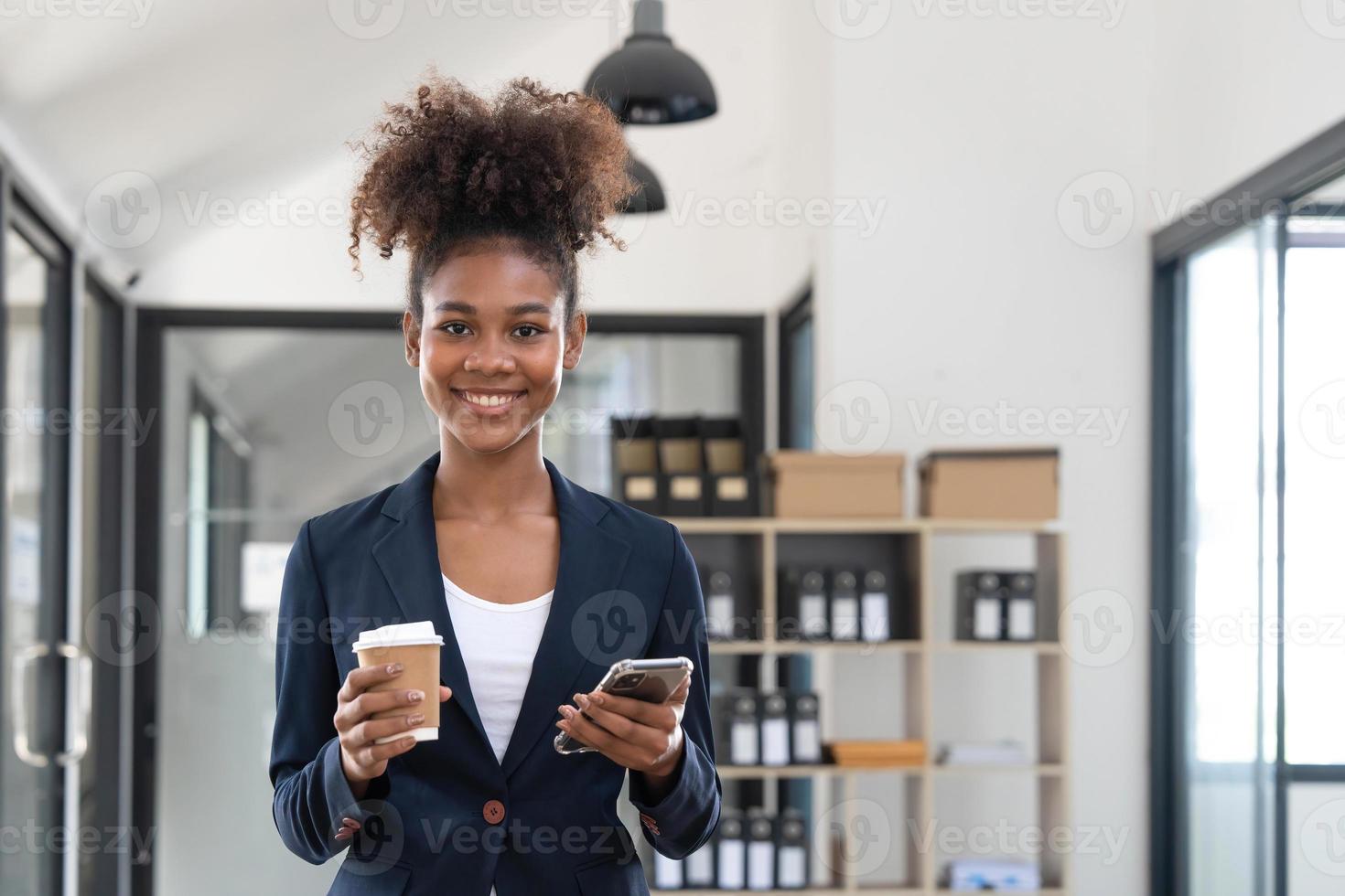 Aufnahme einer lächelnden jungen Geschäftsfrau, die Nachrichten mit dem Handy sendet, das auf dem Schreibtisch im Büro sitzt. foto