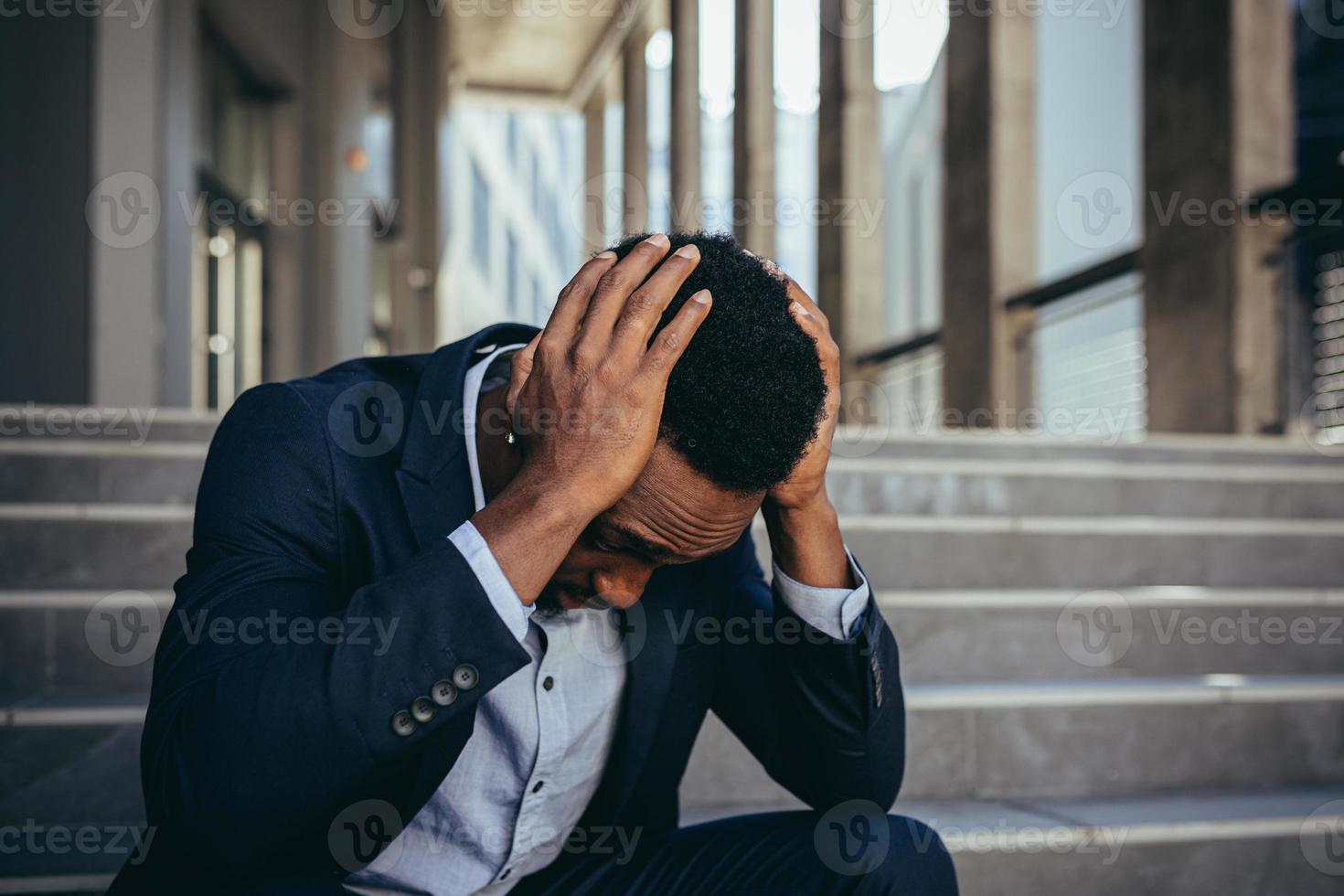 männlicher büroangestellter müde nach der arbeit, afroamerikaner hat starke kopfschmerzen, sitzt foto