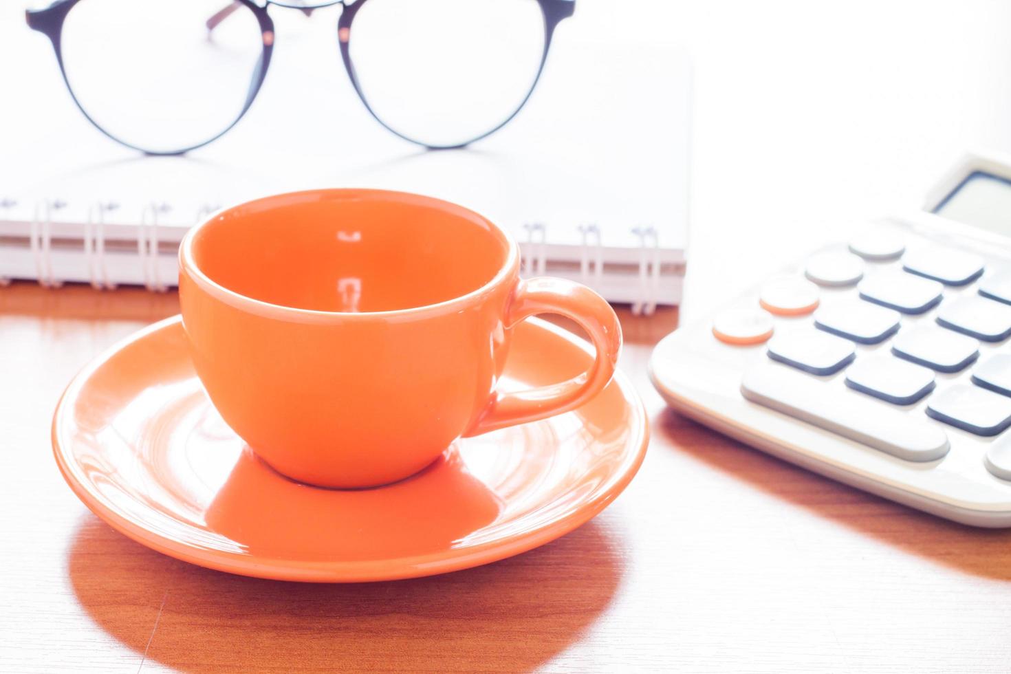 orange Kaffeetasse mit Taschenrechner und Gläsern foto