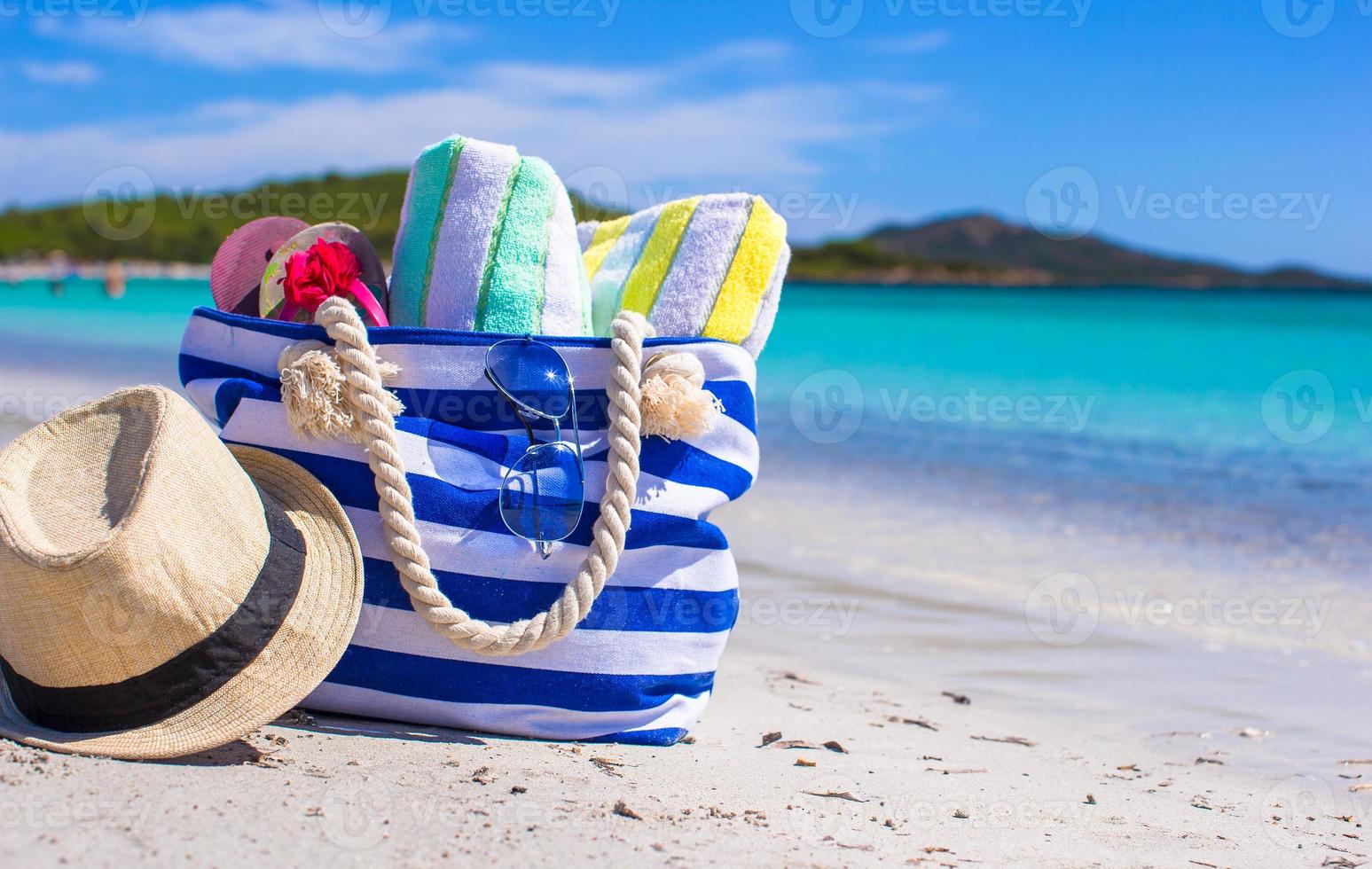 blaue Tasche, Strohhut, Flip Flops und Handtuch am weißen Strand foto