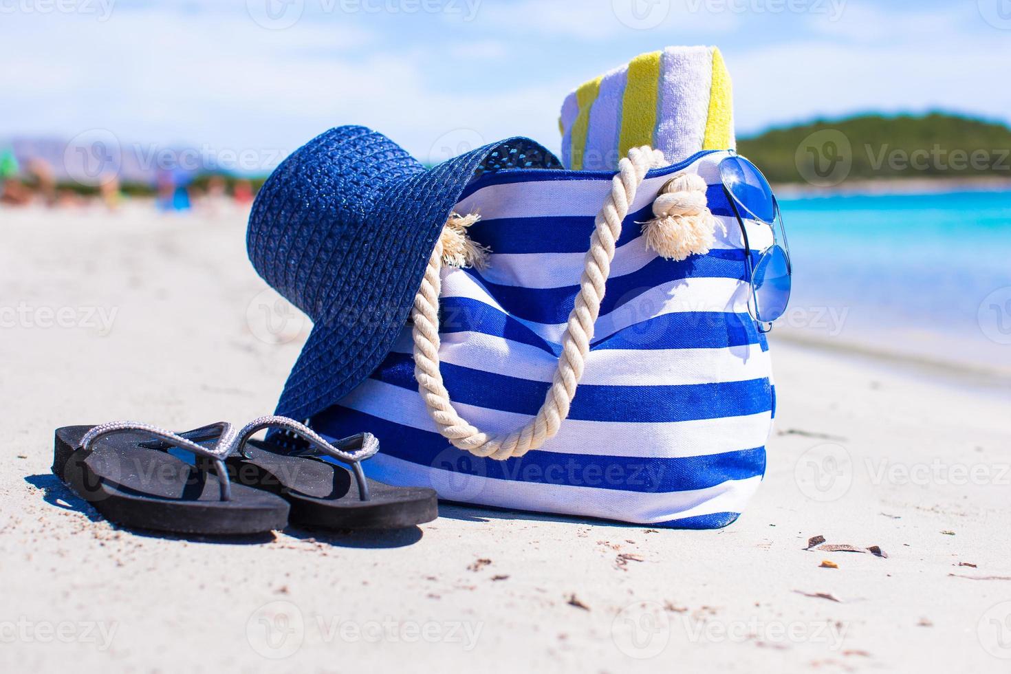 Strohhut, Tasche und Handtuch am weißen tropischen Strand foto