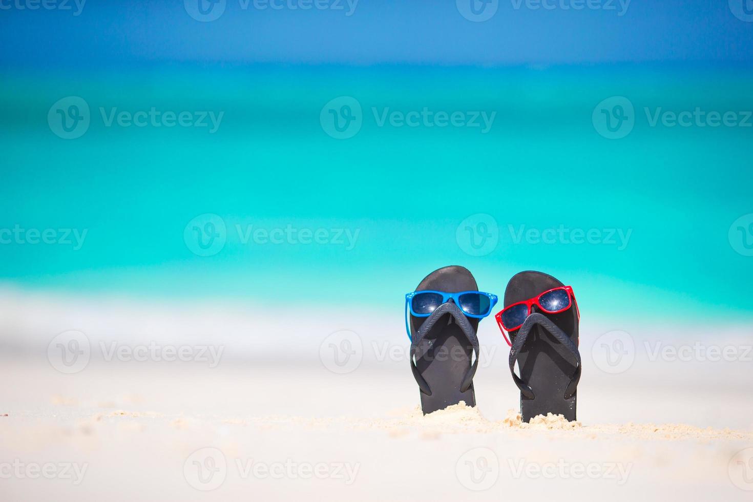 Sommer-Flip-Flops mit Sonnenbrille am weißen Strand foto