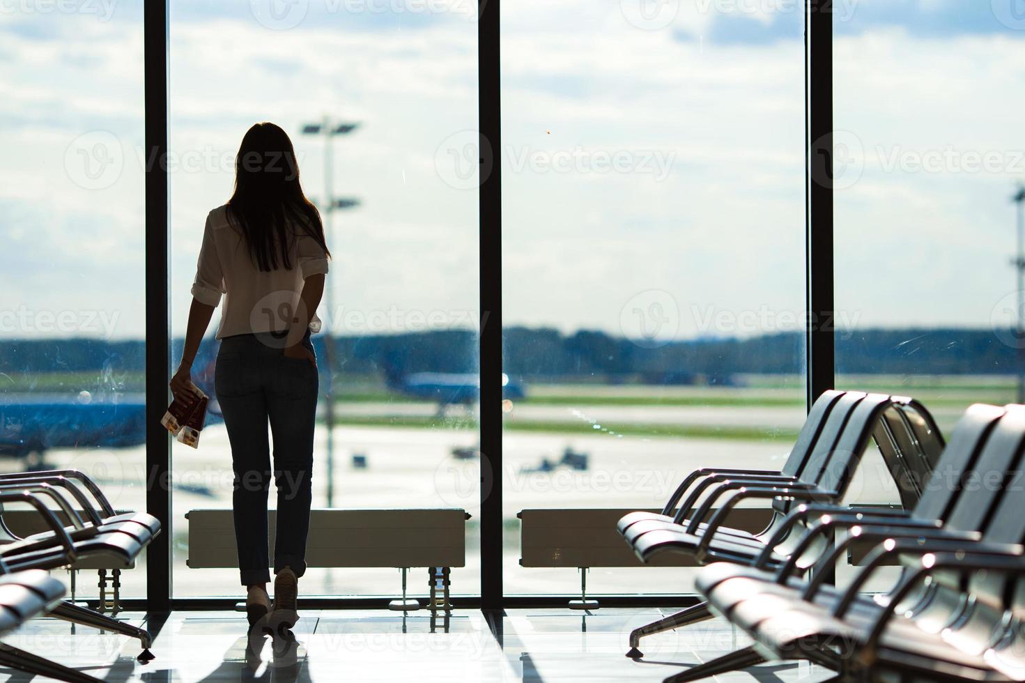 junge Frau am Fenster in einer Flughafenlounge, die auf Flugflugzeuge wartet foto