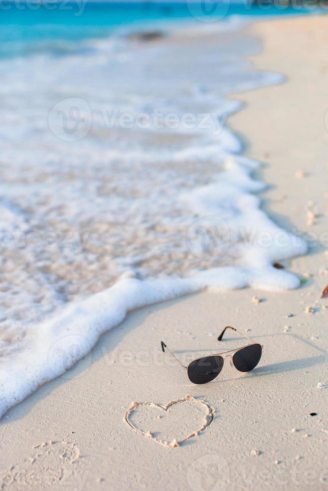 Nahaufnahme von Sonnenbrille und Herz am tropischen Strand foto