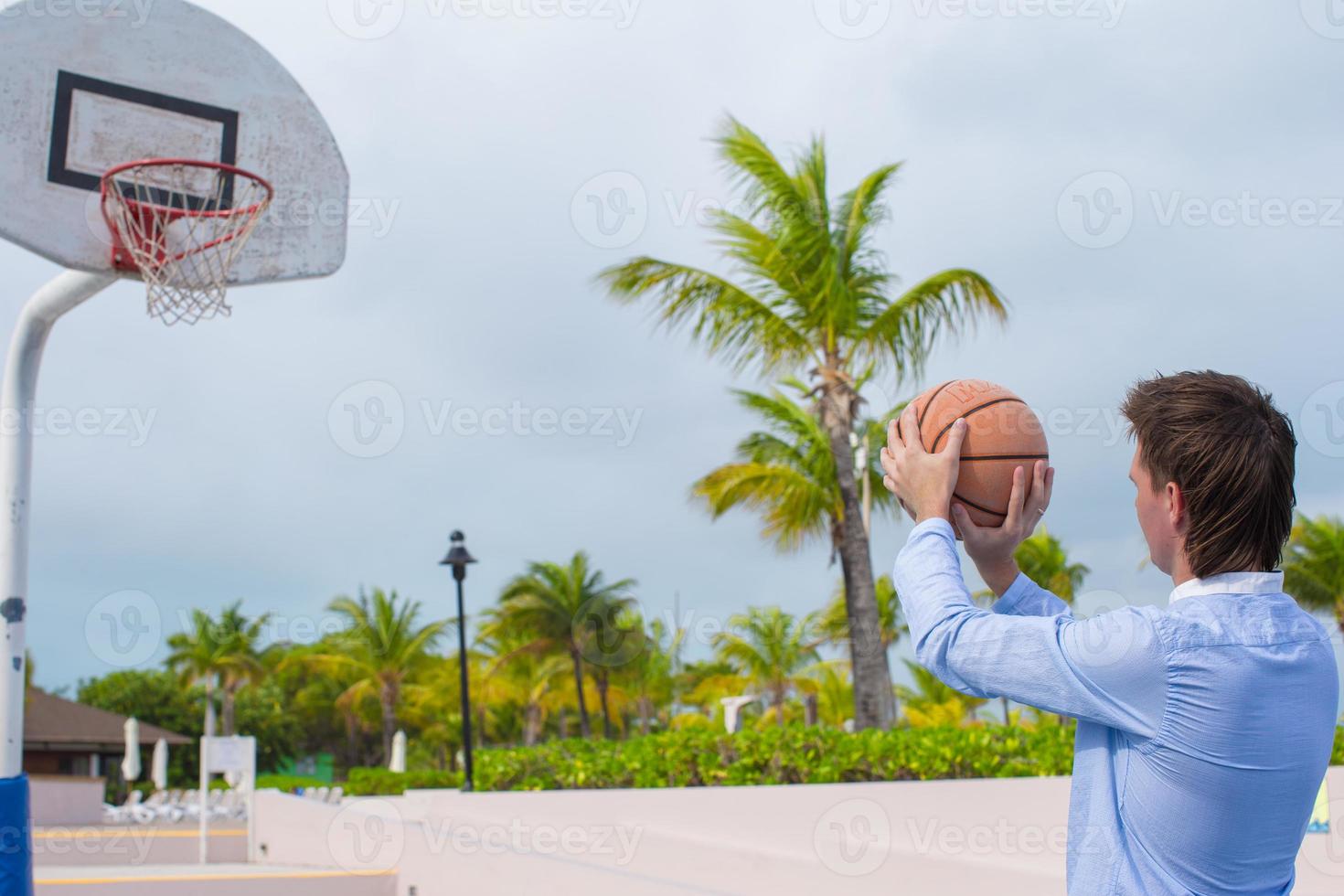 junger Mann, der draußen im exotischen Resort Basketball spielt foto