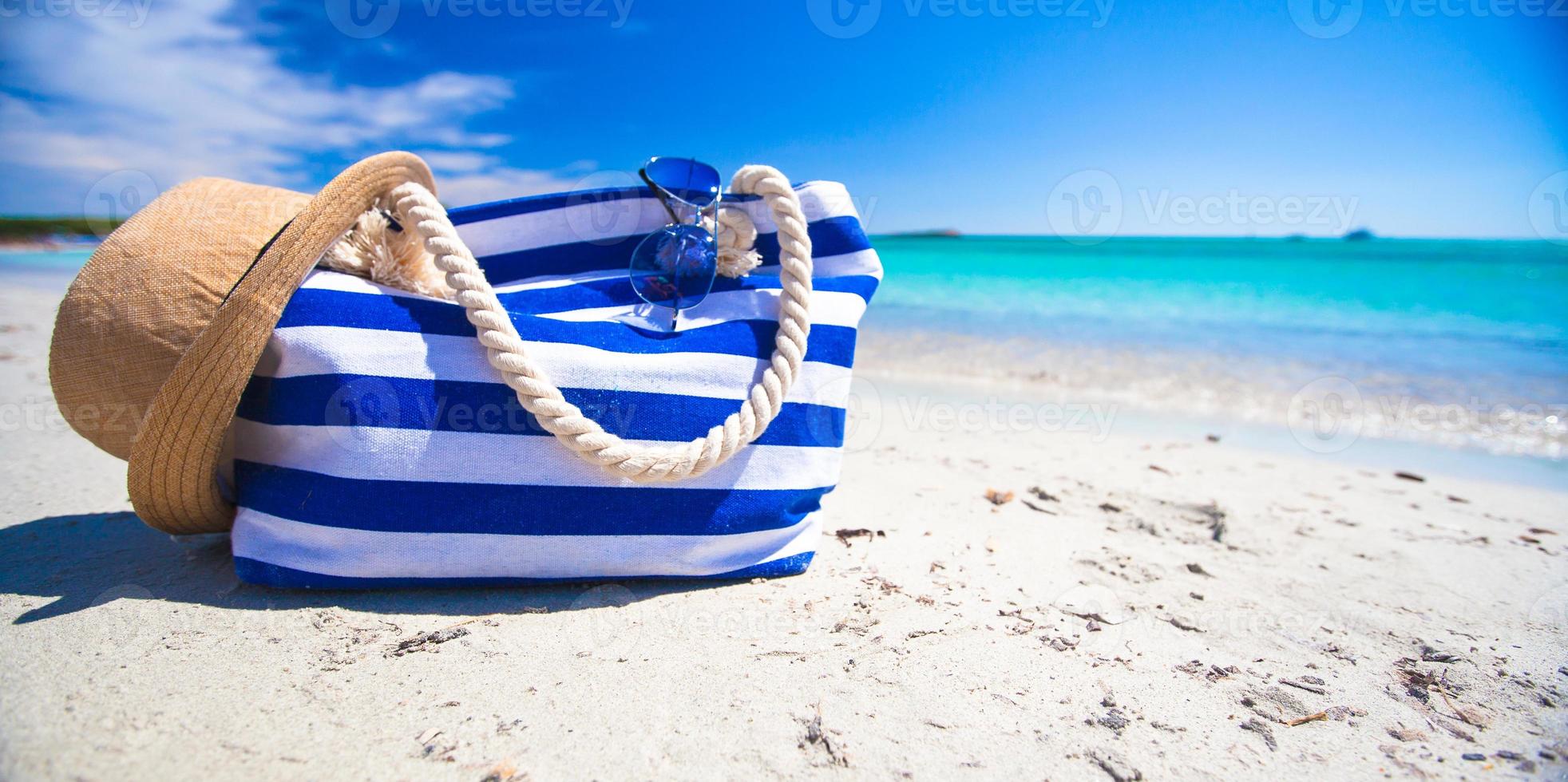 Streifentasche, Strohhut, Sonnencreme und Handtuch am weißen tropischen Strand foto