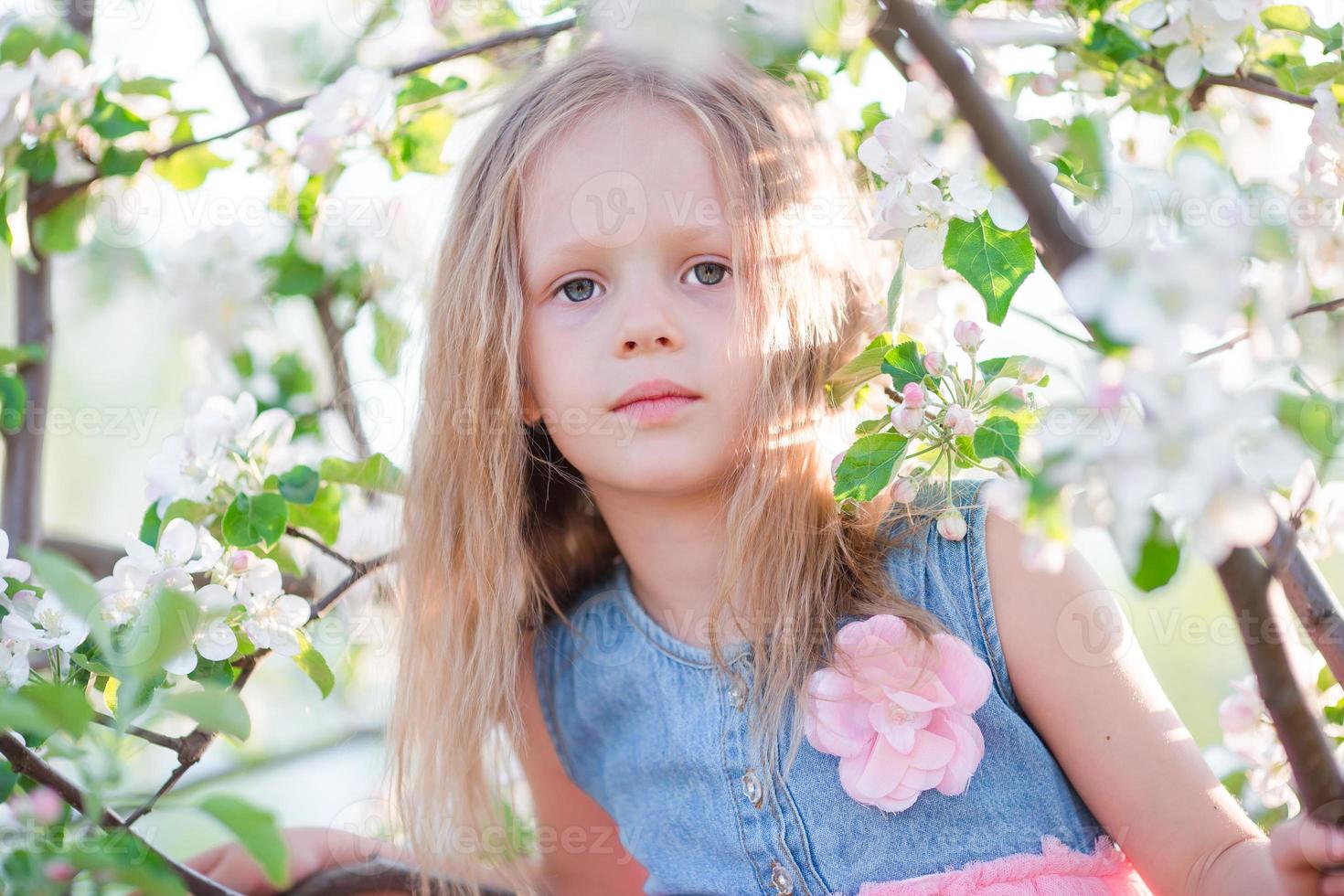 Porträt eines kleinen Mädchens im blühenden Apfelbaumgarten am Frühlingstag foto