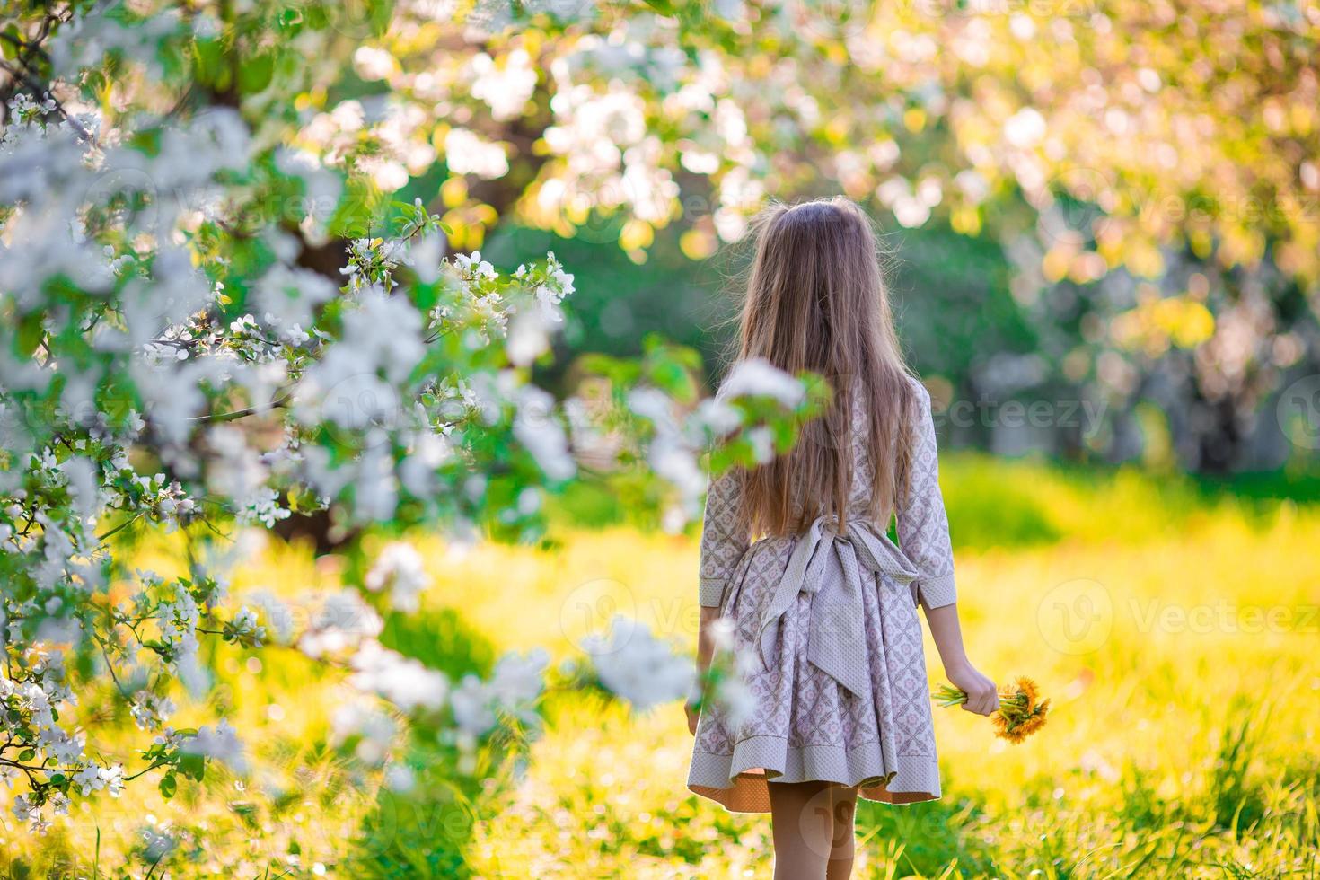 entzückendes kleines Mädchen im blühenden Apfelbaumgarten am Frühlingstag foto