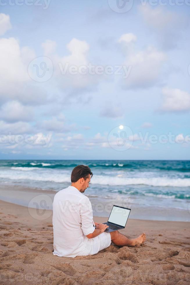 Mann mit Laptop am Strand bei Sonnenuntergang foto