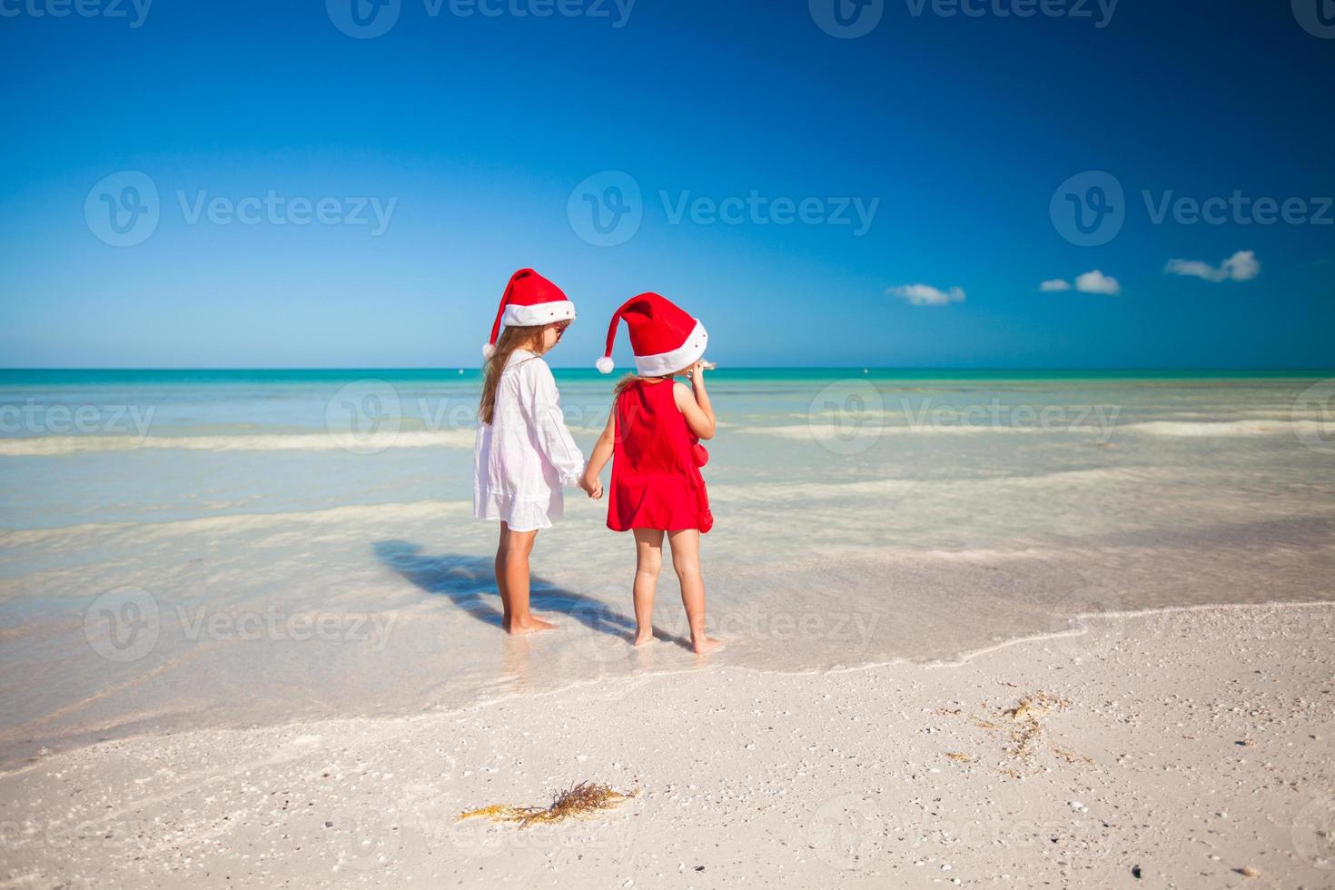 Rückansicht von kleinen süßen Mädchen in Weihnachtsmützen am exotischen Strand foto