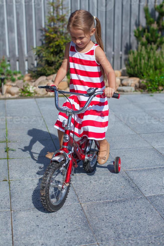 Kleines süßes Mädchen fährt Fahrrad im Kleid im Hof foto