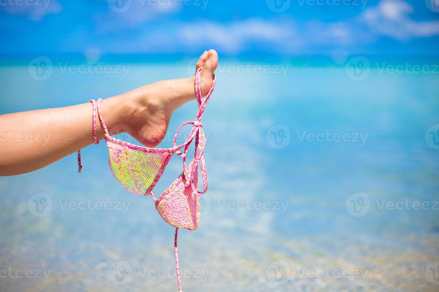 Rosafarbener Badeanzug am weiblichen Bein am weißen tropischen Strand foto