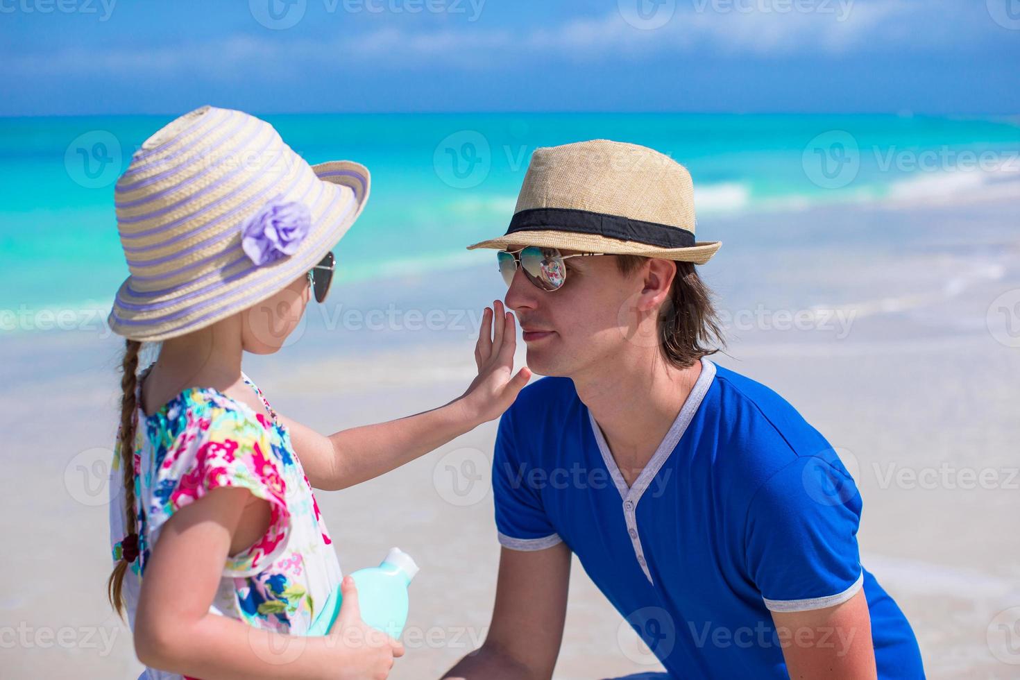 Vater bewirbt sich schützend Sahne zu ihr Tochter Gesicht beim das Strand.  Mann Hand halten Sonnenschutz Lotion auf Baby Gesicht. süß wenig Mädchen  mit ein Sonne Block durch das Meer . Kopieren