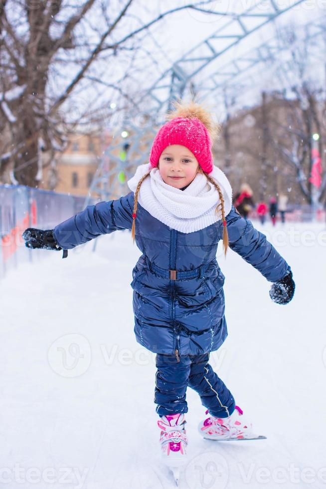 entzückendes kleines Mädchen, das draußen auf der Eisbahn Schlittschuh läuft foto