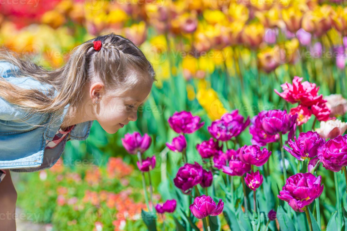 Kleines entzückendes Mädchen, das am Sommertag bunte Tulpen riecht foto