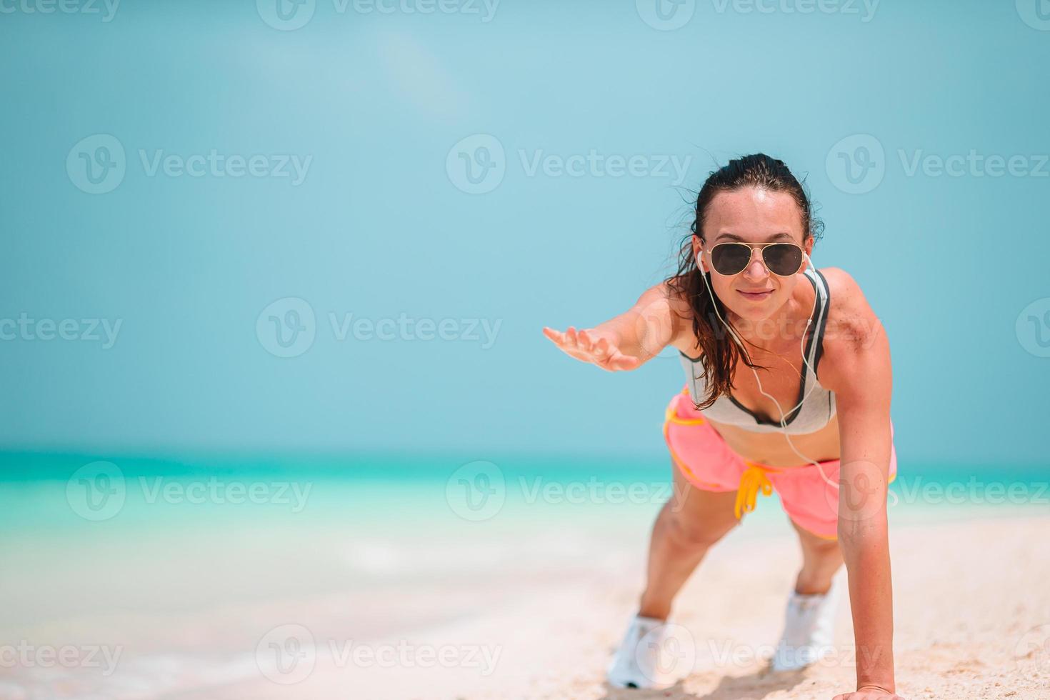 Fitte junge Frau, die in ihrer Sportkleidung Übungen am tropischen weißen Strand macht foto