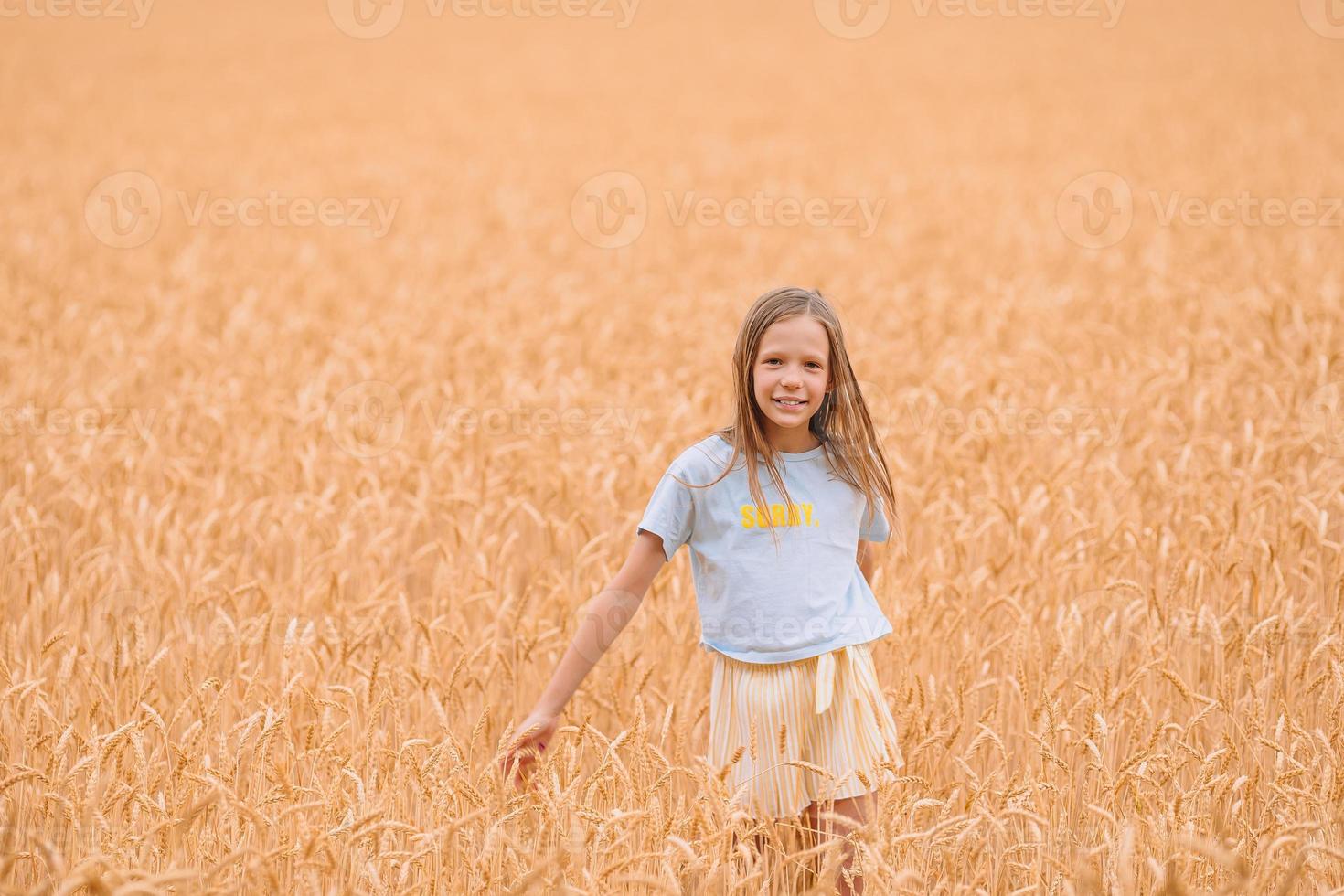 entzückendes Vorschulmädchen, das an warmen und sonnigen Sommertagen glücklich im Weizenfeld spazieren geht foto