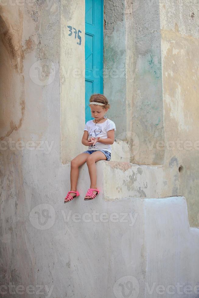 entzückendes kleines mädchen, das auf den stufen des alten hauses im dorf emporio, santorini, griechenland sitzt foto