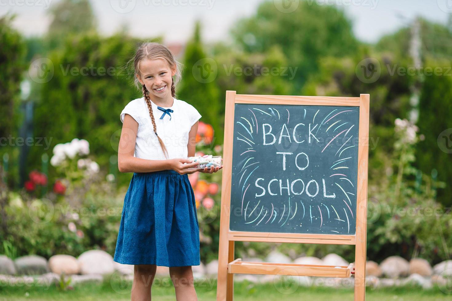 glückliches kleines Schulmädchen mit einer Tafel im Freien foto