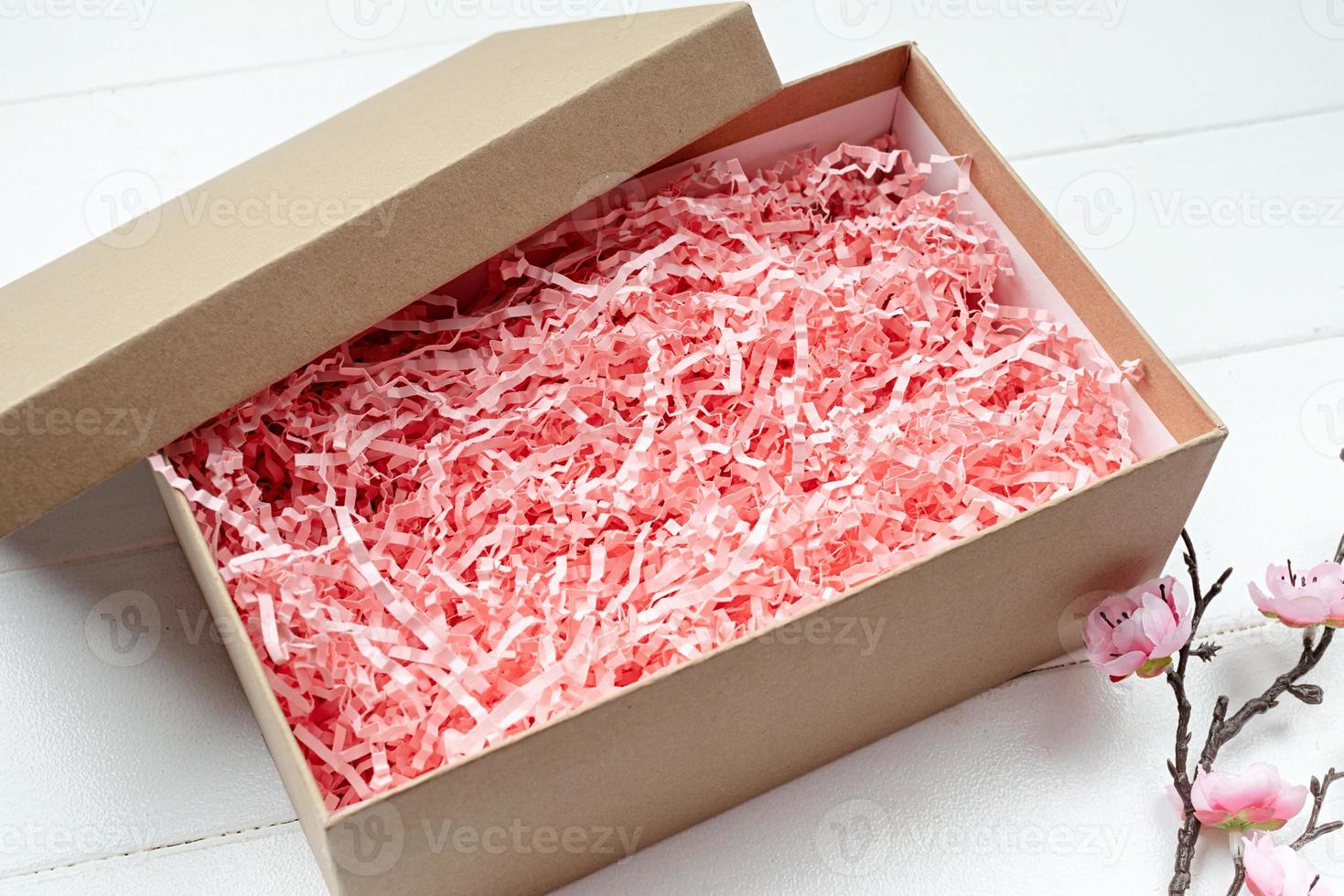 geschredderte rosa papierverpackungsmaterialstruktur in einer handwerksbox mit sakura-zweig, mockup-design foto