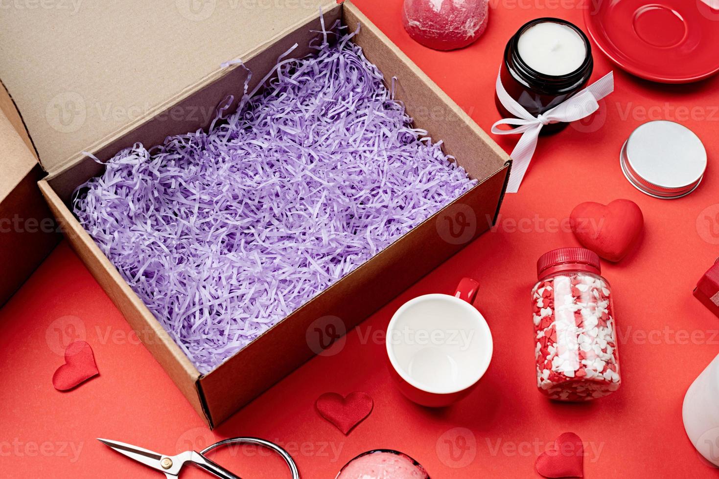 saisonale geschenkbox zum valentinstag mit kerze, roter tasse und herzförmigen süßigkeiten auf rotem hintergrund foto