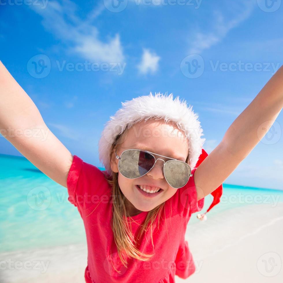 kleines entzückendes mädchen in roter weihnachtsmütze viel spaß am strand foto