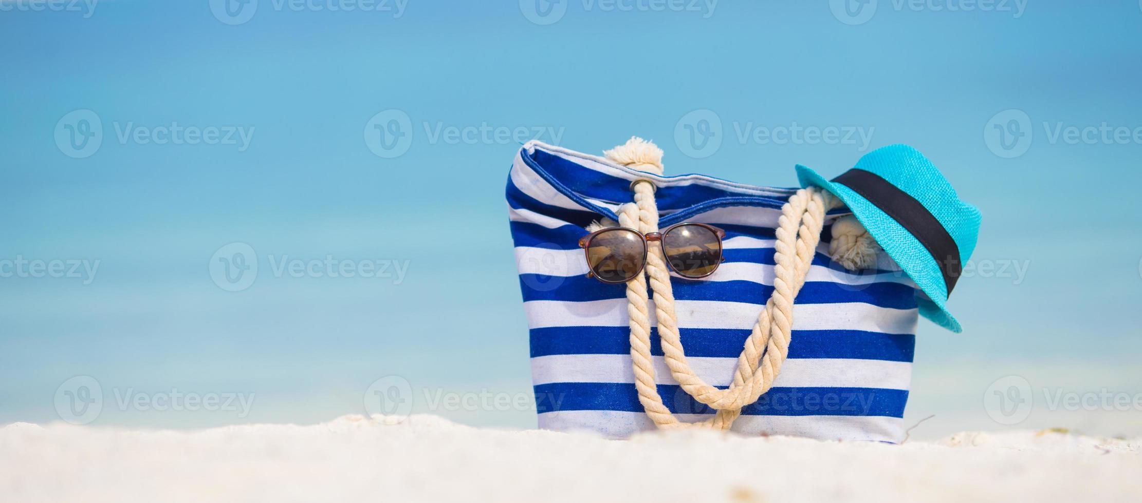 Strandzubehör - blaue Tasche, Strohhut, Sonnenbrille am weißen Strand foto