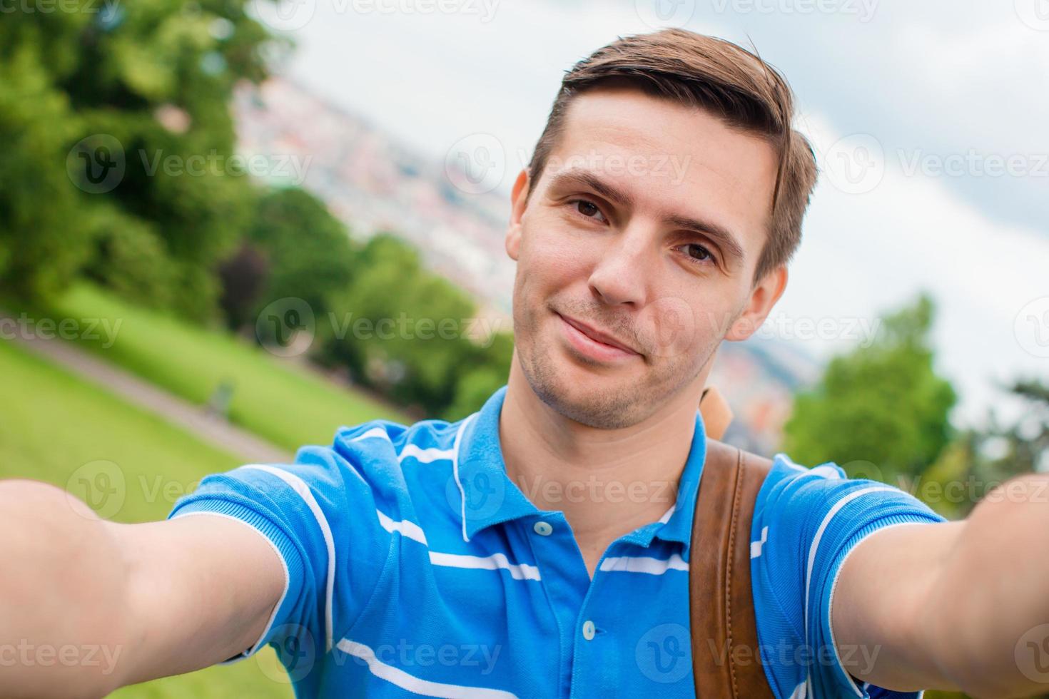 junger kaukasischer mann, der selfie im hintergrund der europäischen altstadt per handy vom beobachtungsplatz aus macht foto
