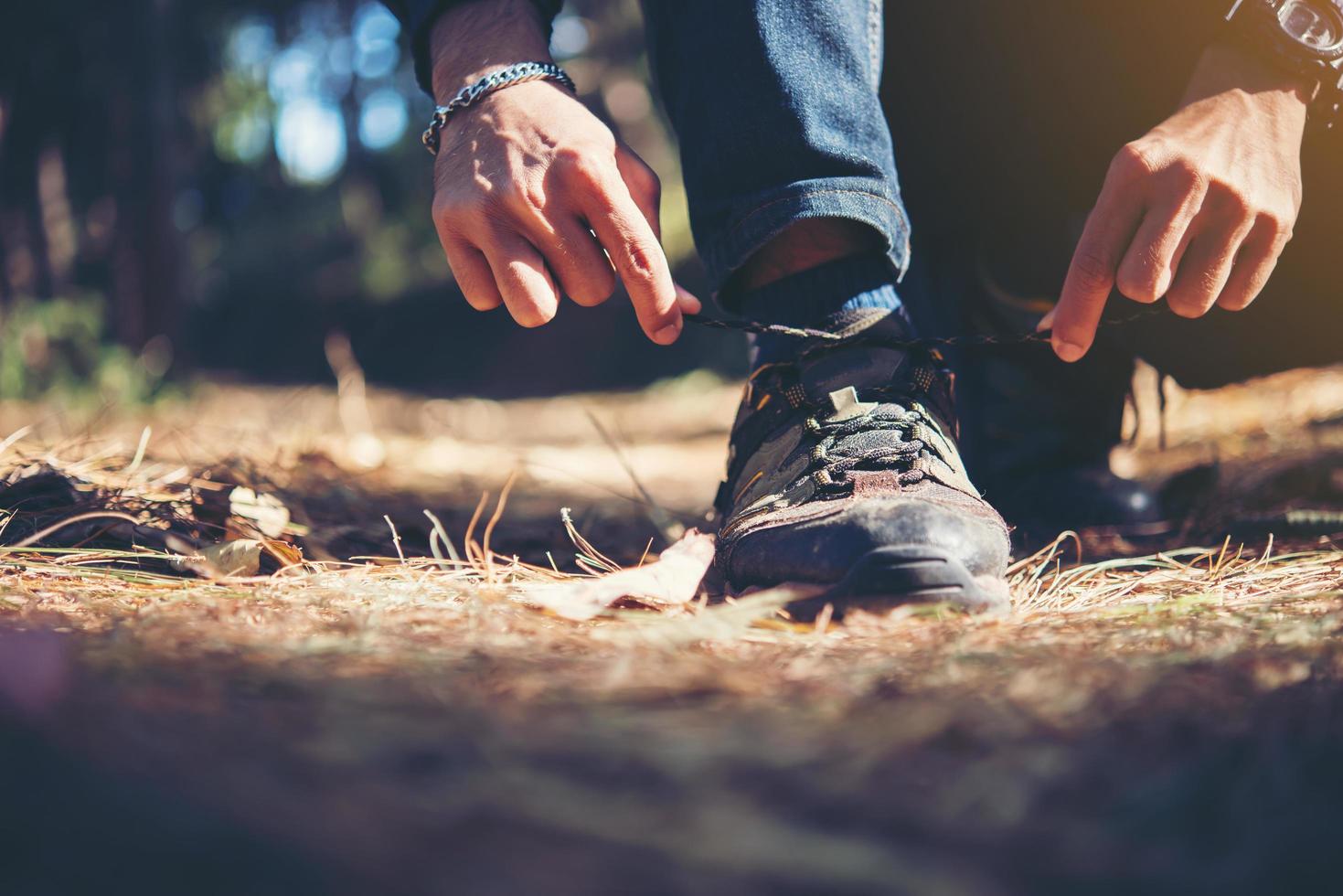 Der junge Wanderer bindet seine Schnürsenkel, während er im Wald wandert foto