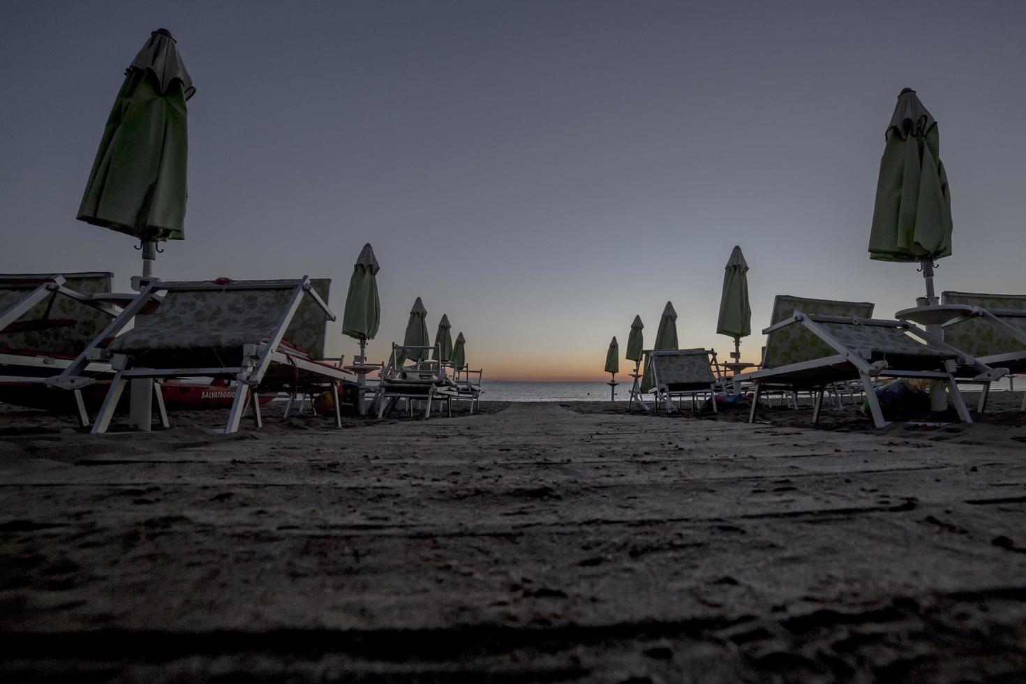 Liegestühle mit Sonnenschirmen am Strand bei Sonnenuntergang foto