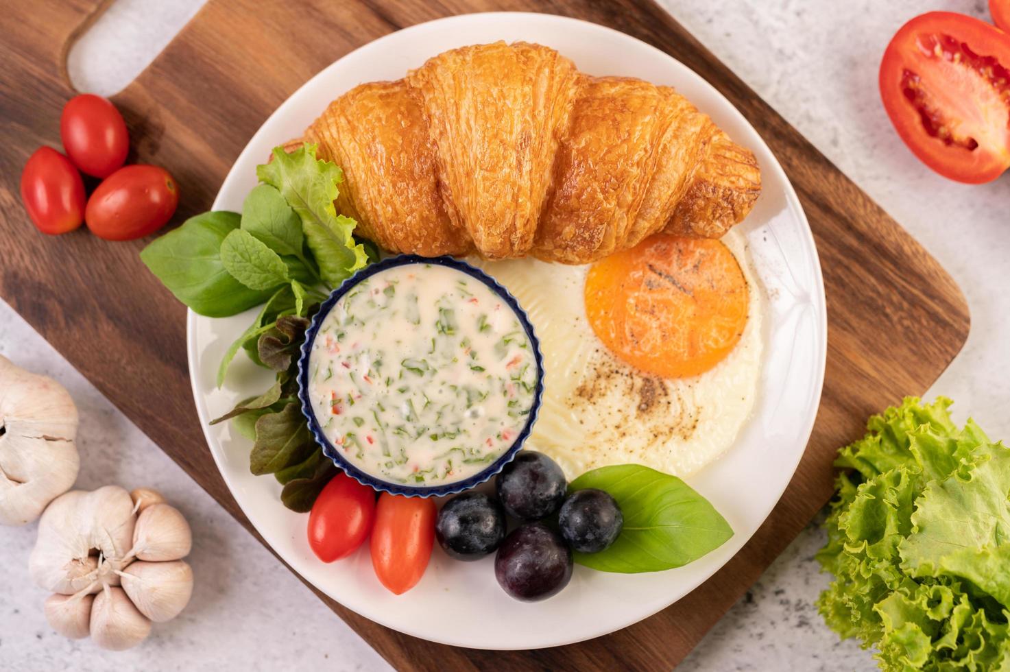 Croissant, Spiegelei, Salatdressing, schwarze Trauben und Tomaten foto