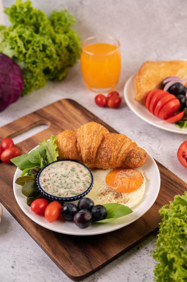 Croissant, Spiegelei, Salatdressing, schwarze Trauben und Tomaten foto