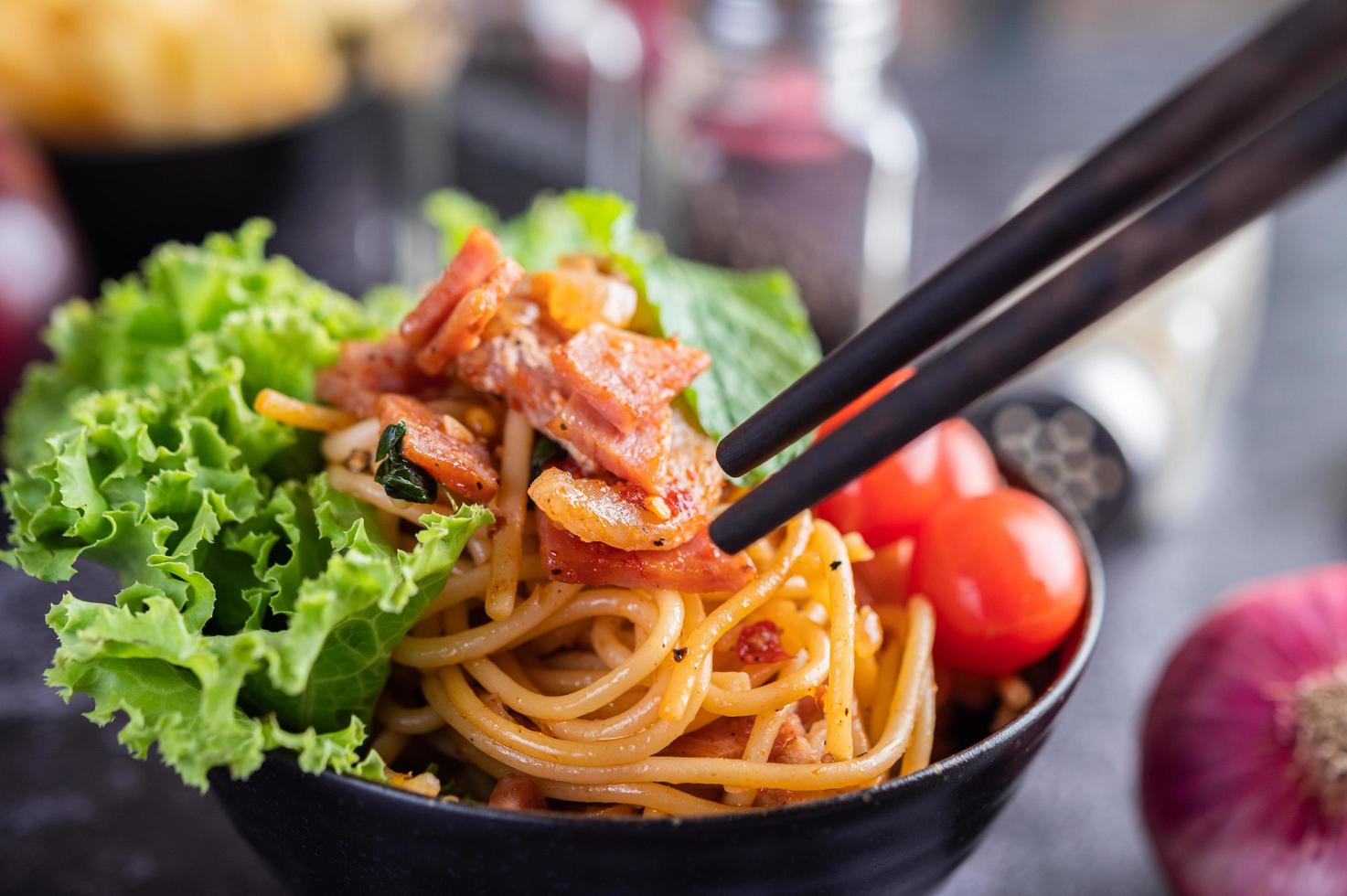 Spaghetti in einer schwarzen Tasse mit Tomaten und Salat. foto