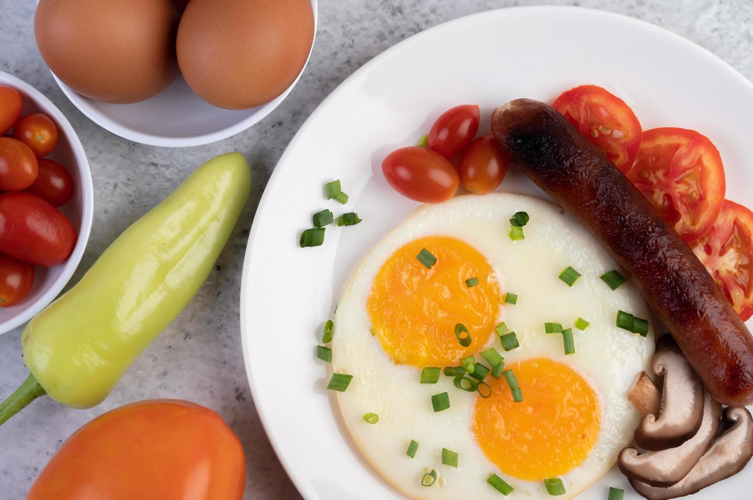 Frühstücksteller mit Spiegeleiern, Tomaten, chinesischer Wurst und Pilzen foto