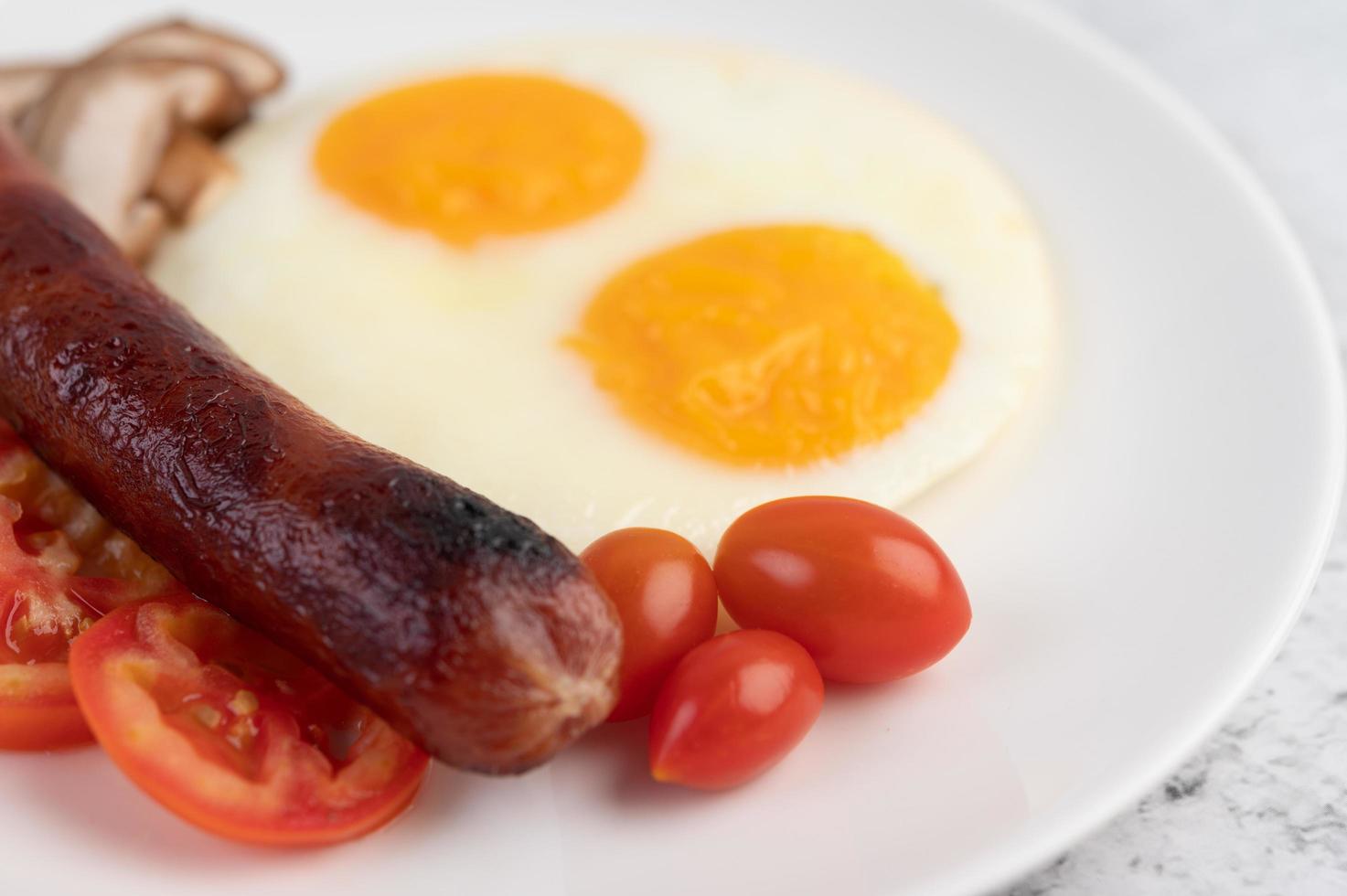 Frühstücksteller mit Spiegeleiern, Tomaten, chinesischer Wurst und Pilzen foto