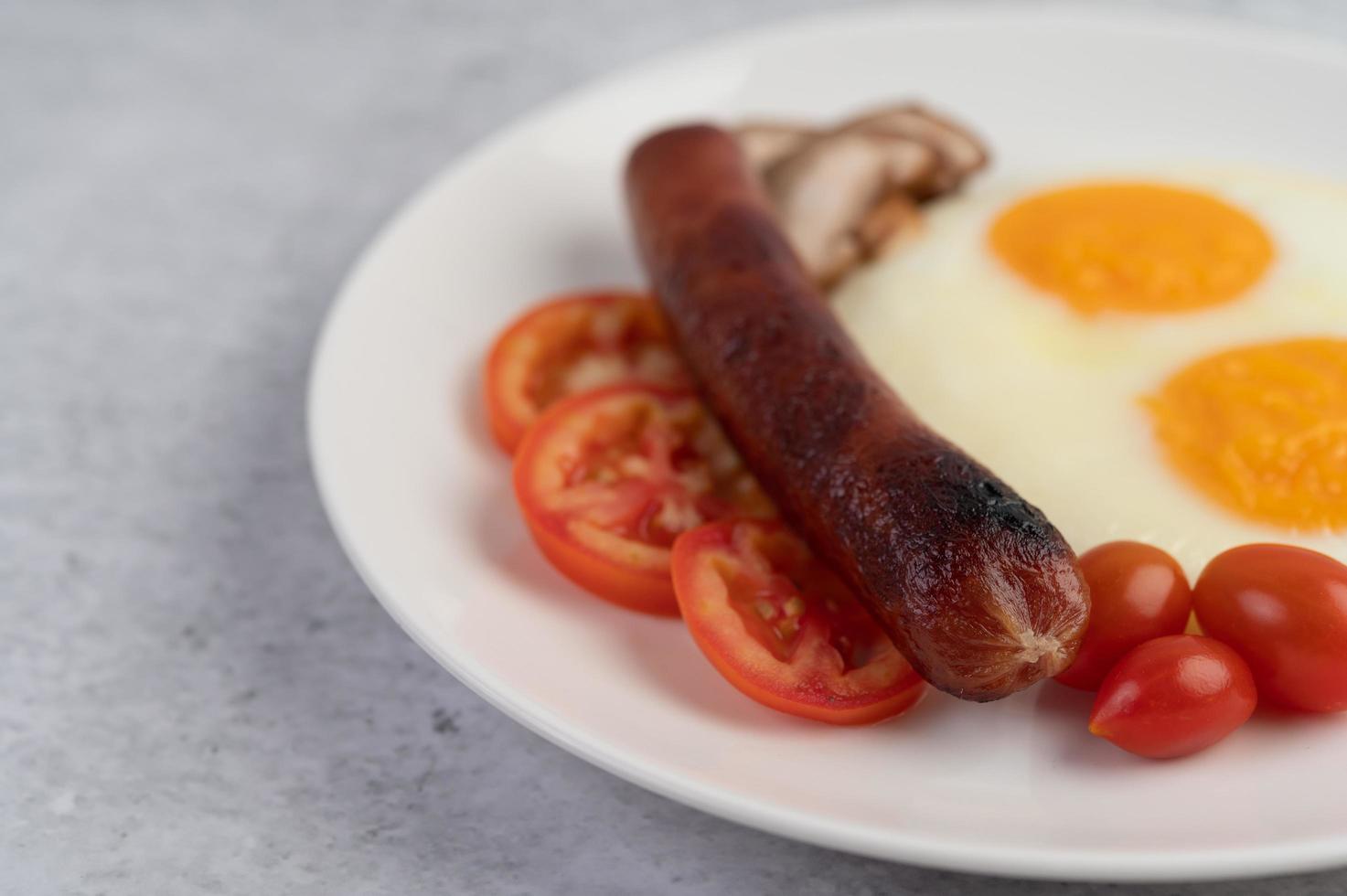 Frühstücksteller mit Spiegeleiern, Tomaten, chinesischer Wurst und Pilzen foto