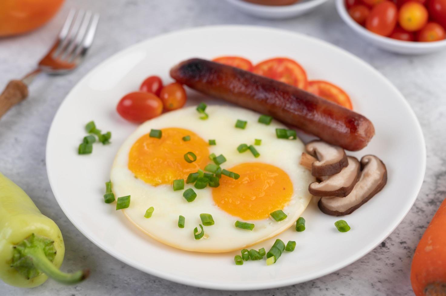 Frühstücksteller mit Spiegeleiern, Tomaten, chinesischer Wurst und Pilzen foto