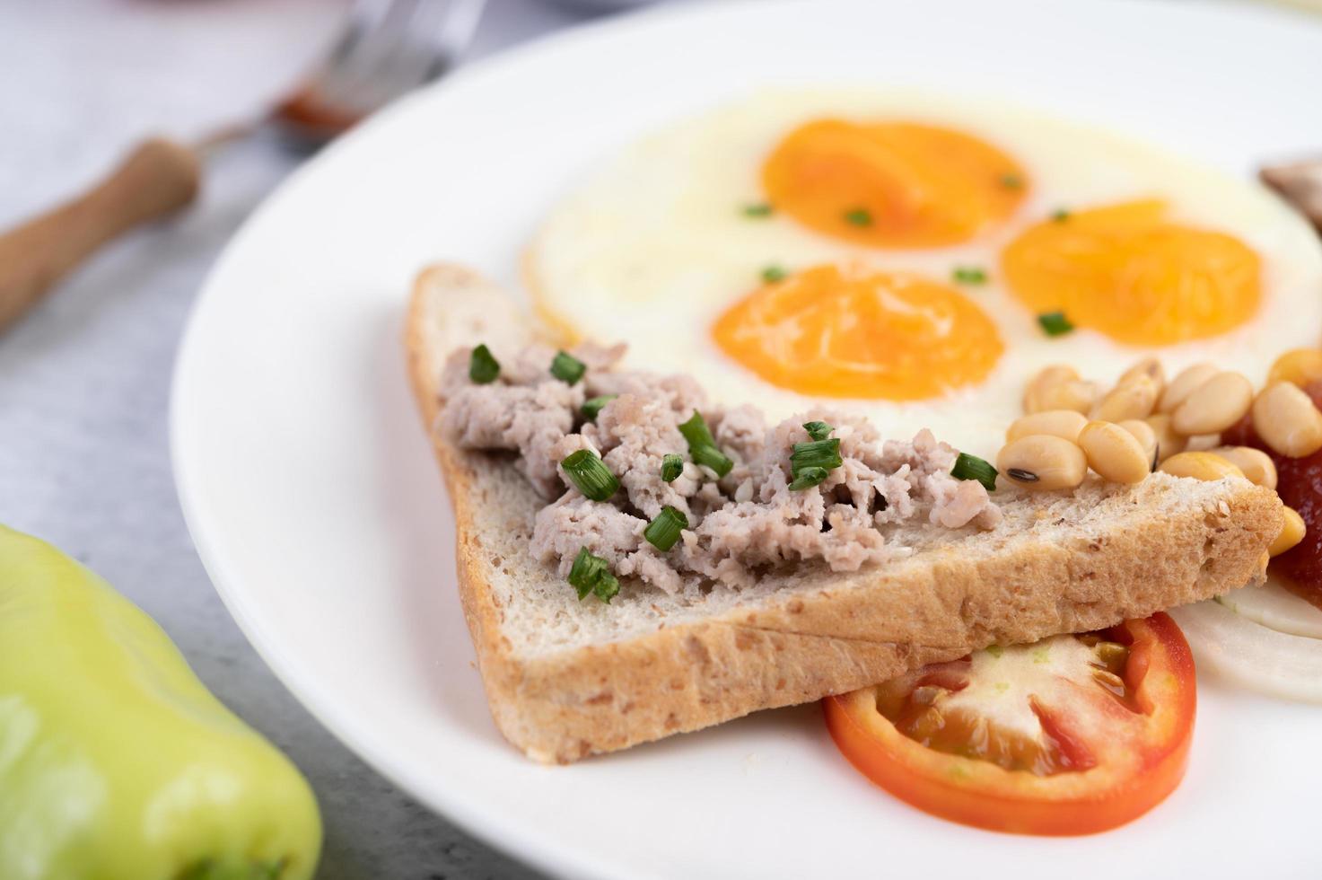 Spiegeleier, Wurst, gehacktes Schweinefleisch, Brot und rote Bohnen foto