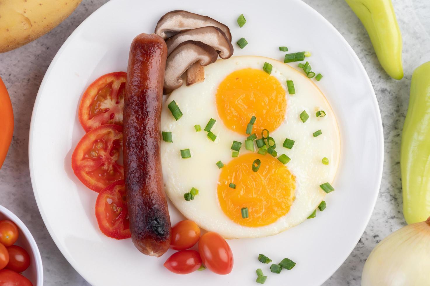 Frühstücksteller mit Spiegeleiern, Tomaten, chinesischer Wurst und Pilzen foto