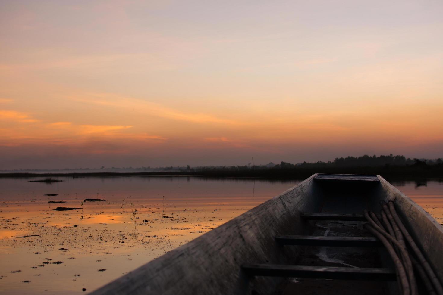 Holzboot am Fluss mit dem Sonnenuntergang festgemacht. foto