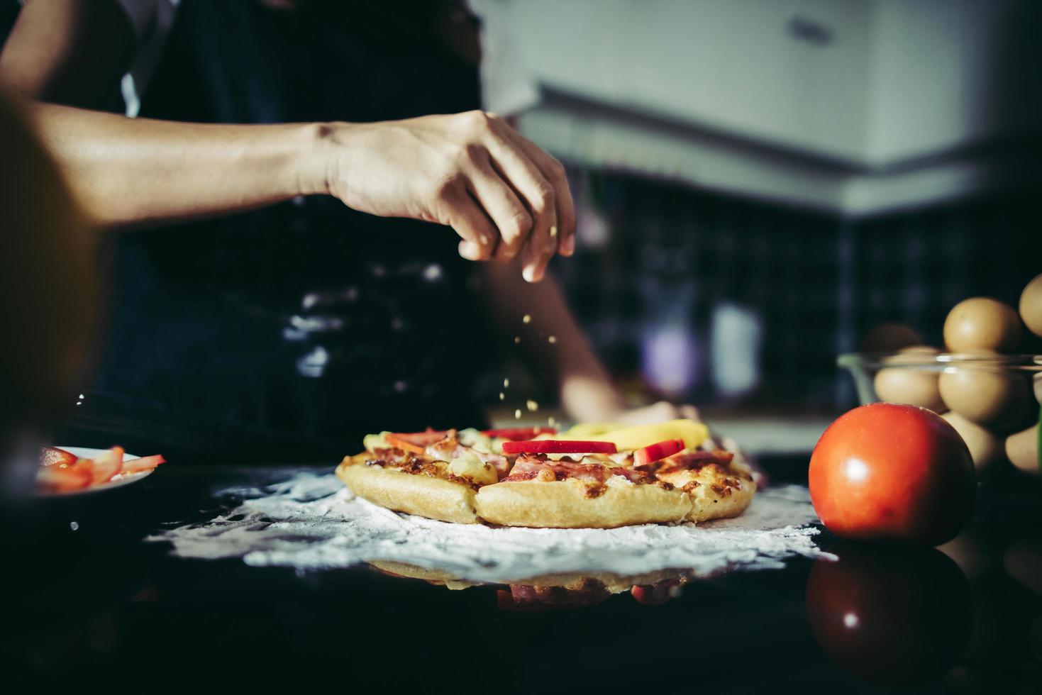 Nahaufnahme einer Hand, die Oregano über eine Pizza legt foto