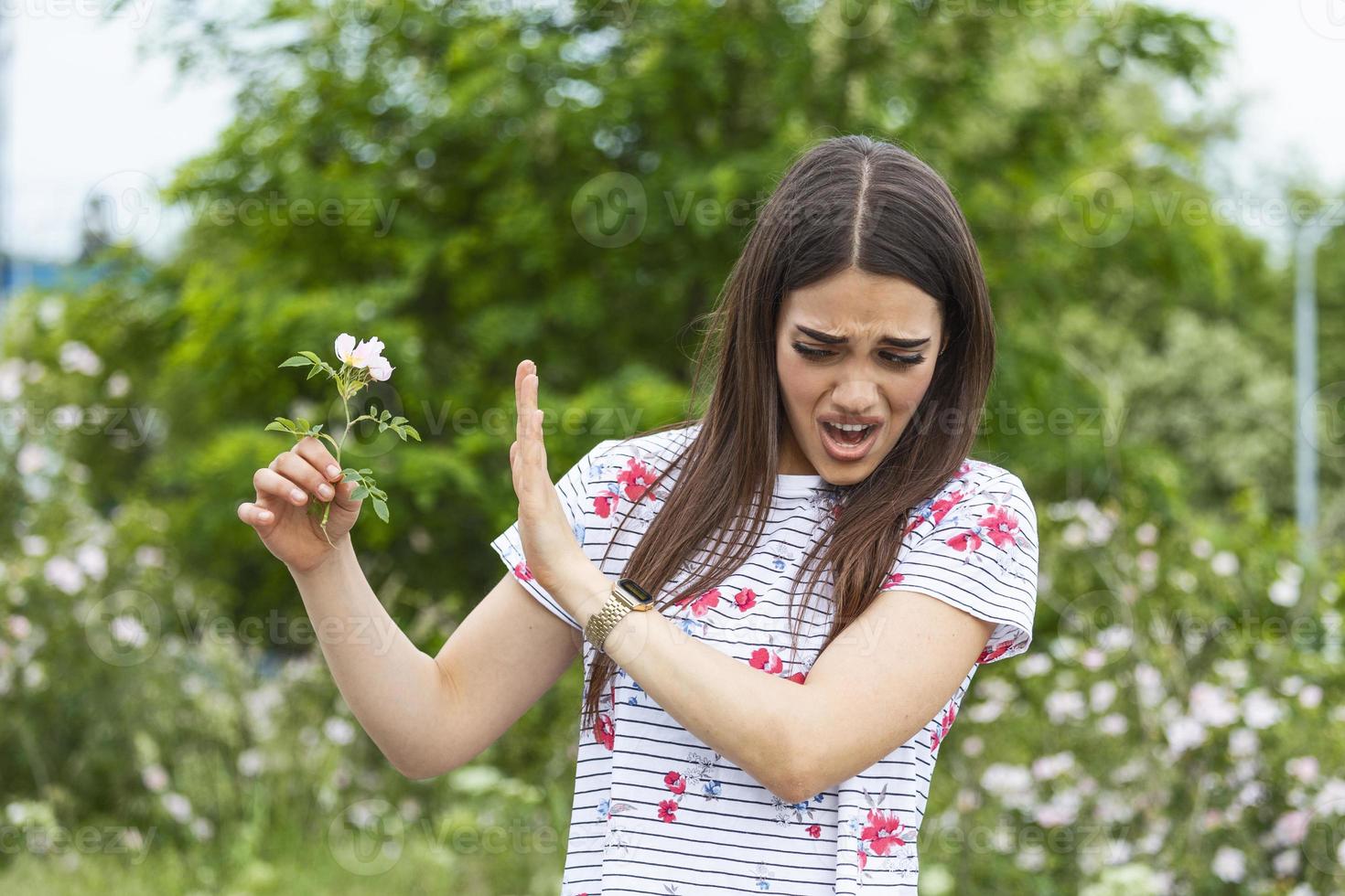 junge Frau mit Pollenallergie, die eine Blume hält und Nein sagt. junge Frau mit Pollen- und Gräserallergie. blühende Bäume im Hintergrund. frühling saisonale allergien und gesundheitliche probleme. foto