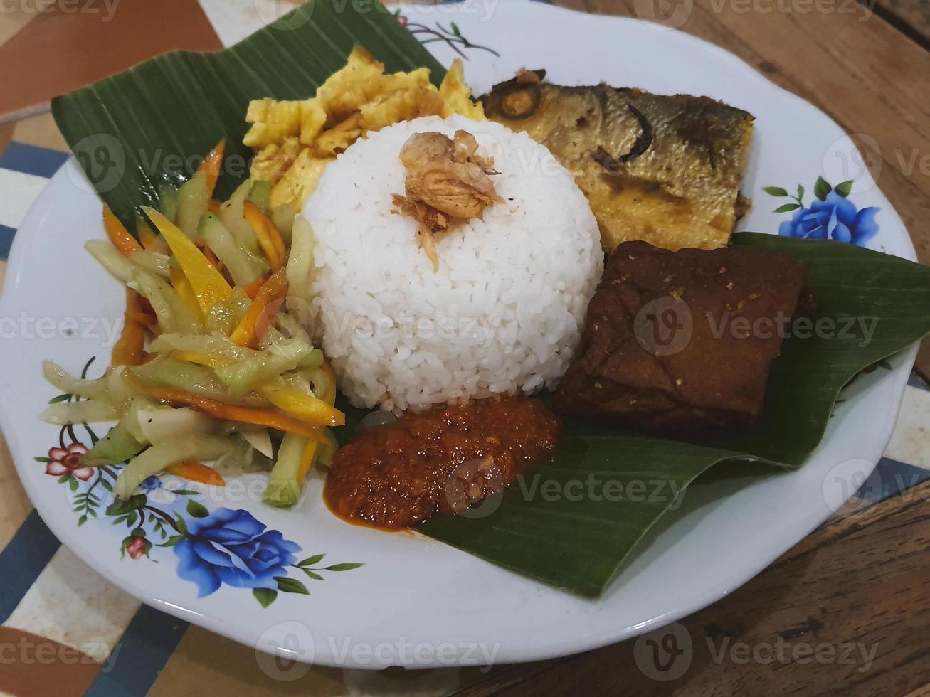 eine Portion Nasi Kucing komplett mit gebratenem Milchfischkopf, Tofu, serviert auf einem Teller mit Bananenblättern. foto