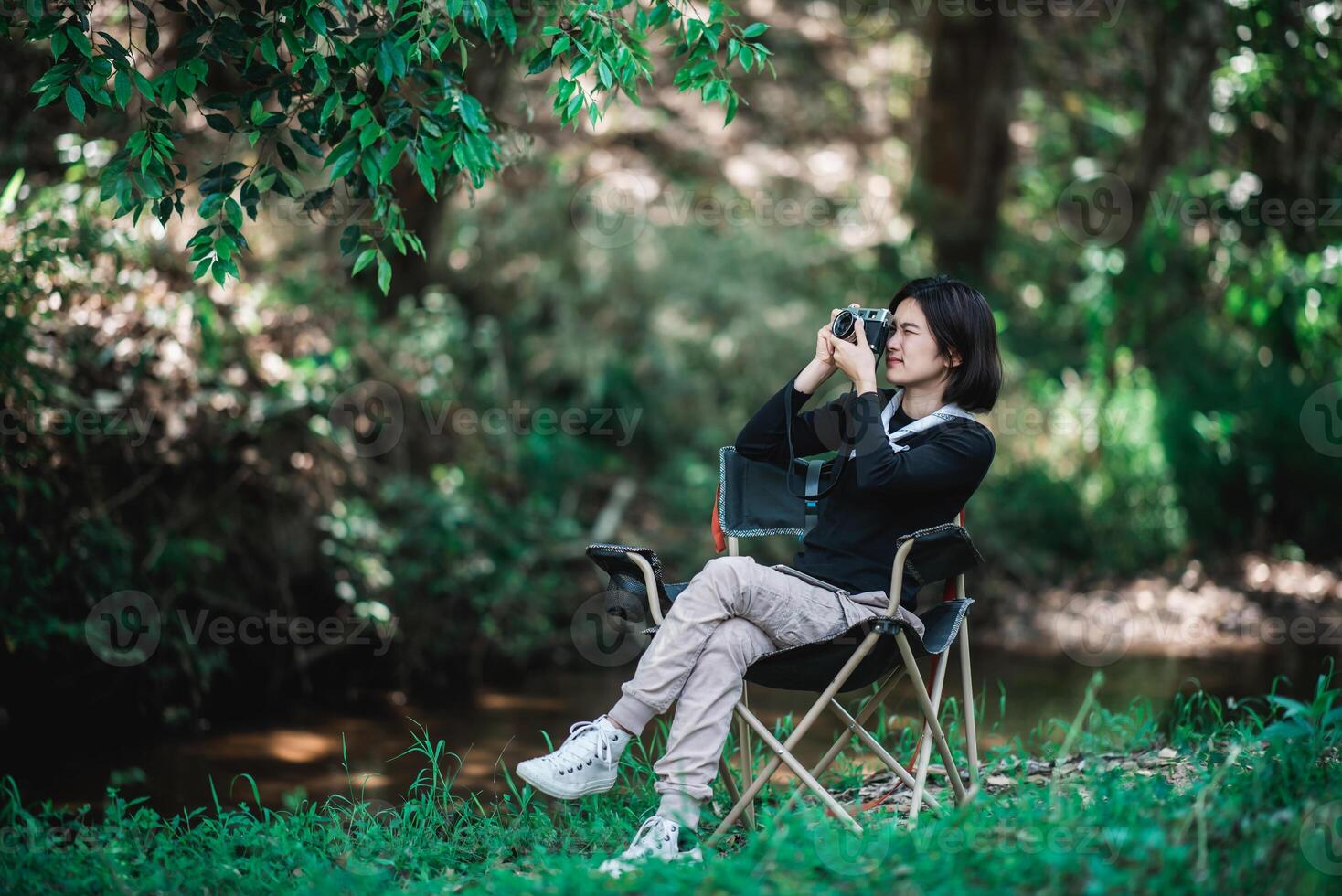 junge hübsche frau benutzt kamera, die foto im naturpark macht