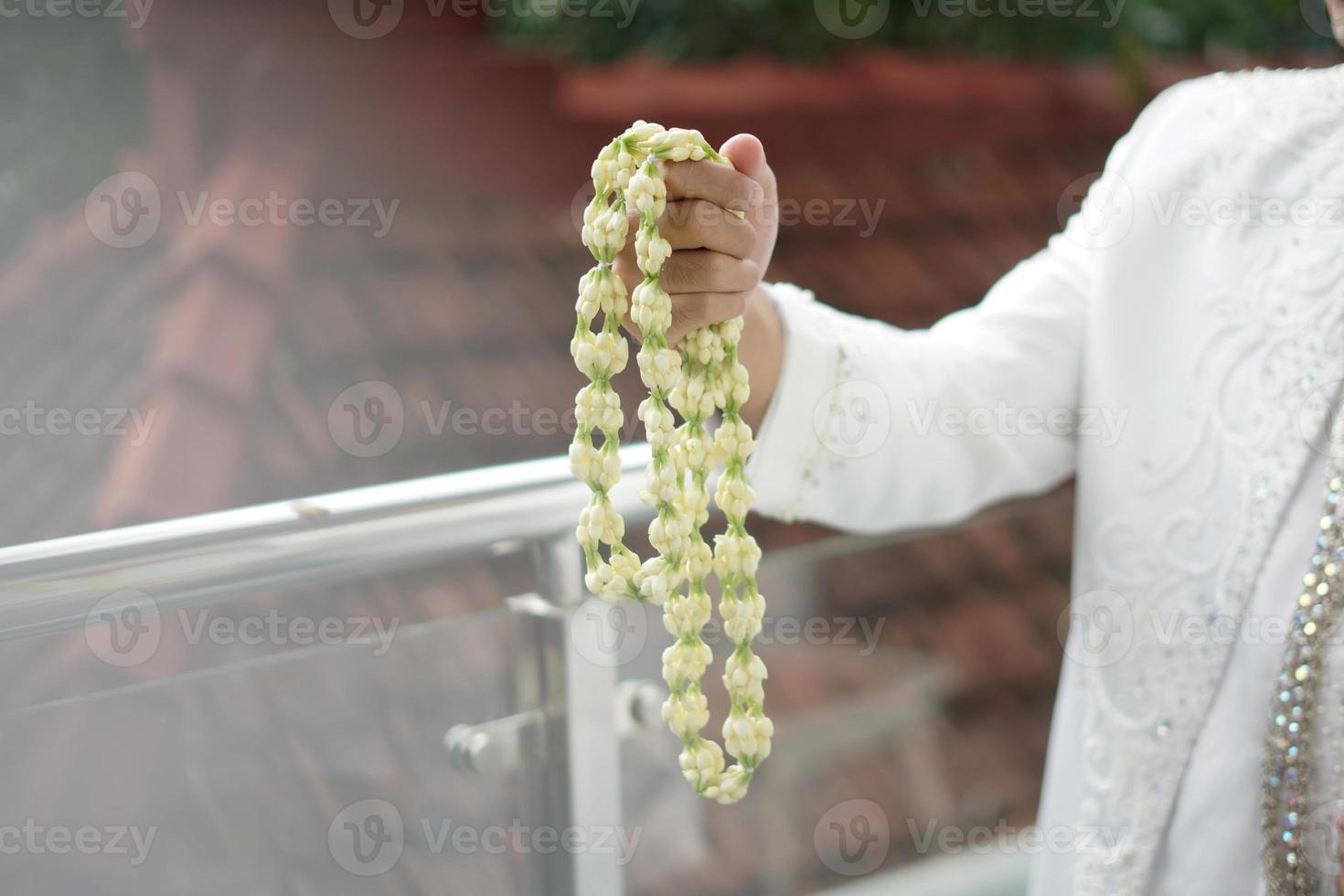 ein Bräutigam, der eine Halskette mit Jasmin- und Magnolienblumen hält foto