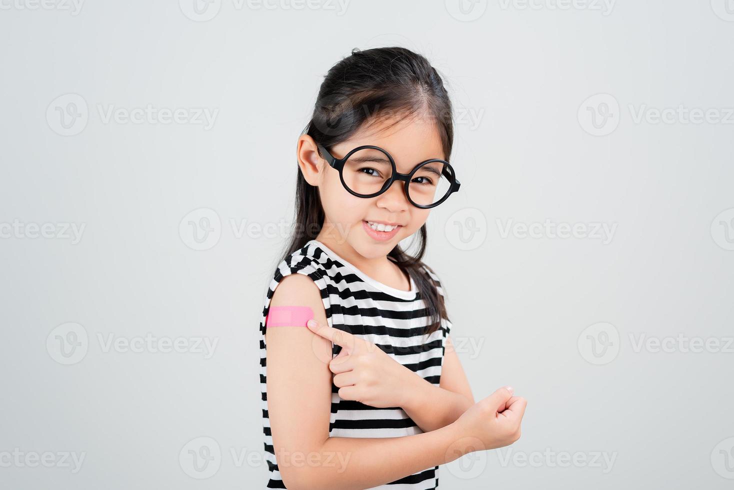 asiatische kleine mädchen tragen eine brille, die ihren arm mit verband nach der virusimpfstoffimpfung zeigt glückliches kind und kinderimpfungskampagne. schützen sie ihr kind mit einem impfkonzept foto